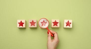 five red stars and a hand with a plastic magnifier on a green background. Evaluation of the quality of services and goods, high rating photo