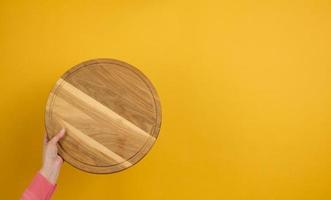 mujer sosteniendo una tabla de pizza de madera redonda vacía en la mano, parte del cuerpo sobre un fondo amarillo foto