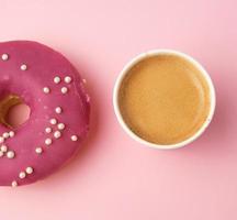 donut rojo redondo y taza de papel con café sobre un fondo rosa foto