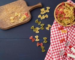 raw pasta in the form of bows in a wooden round plate on a blue wooden background photo