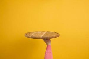 woman holding empty round wooden pizza board in hand, body part  on a yellow background