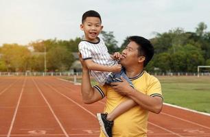 the father carries the child on his shoulders Lovingly looking at the child, smiling happily while exercising around the stadium. Outdoor activities concept with family, father and son. photo