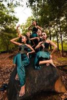 A Group of Asian people in green costumes sitting on a big rock with brown leaves in the background photo