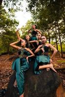 A Group of Asian people in green costumes sitting on a big rock with brown leaves in the background photo