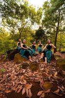 A Group of Asian women takes a vacation to the forest while wearing a green skirt and sitting on a rock photo