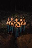 A Bunch of girls in green costumes holding a wooden masks in their hands while standing between the big rocks in front of the forest photo