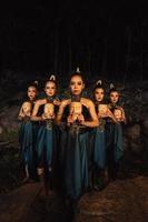 A Bunch of girls in green costumes holding a wooden masks in their hands while standing between the big rocks in front of the forest photo