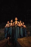 A Bunch of girls in green costumes holding a wooden masks in their hands while standing between the big rocks in front of the forest photo