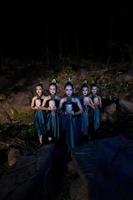 A Group of Javanese women standing in the woods between the rocks while holding a wooden mask photo