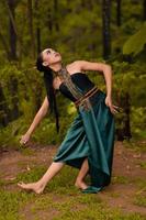 Beautiful Asian woman in a green costume with long black hair dances in the woods photo
