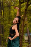 una valiente mujer asiática maquillada con un traje verde y joyas de oro con el bosque al fondo foto