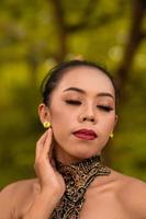 Balinese Woman wearing makeup with red lips while feeling sexy while wearing golden jewelry around her neck during the photo shoot