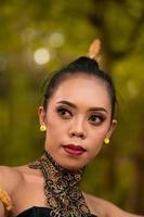 Portrait of a beautiful Asian woman in makeup while dancing in front of the jungle with a black and green costume on her body photo