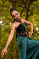 Portrait of a beautiful Asian woman in makeup while dancing in front of the jungle with a black and green costume on her body photo