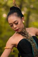 Portrait of a beautiful Asian woman in makeup while dancing in front of the jungle with a black and green costume on her body photo