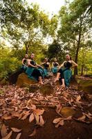 A Group of Asian women takes a vacation to the forest while wearing a green skirt and sitting on a rock photo