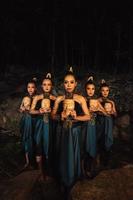 A Bunch of girls in green costumes holding a wooden masks in their hands while standing between the big rocks in front of the forest photo