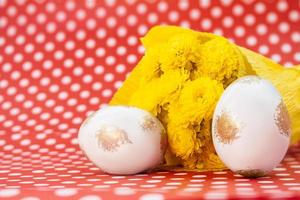 White gold eggs with bouquet of yellow chrysanthemums on red with polka dots background. Easter. Copy space photo