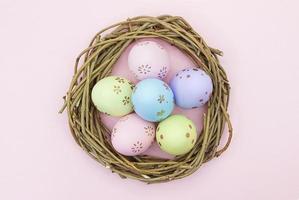 huevos multicolores pintados en nido de ramas de madera sobre fondo rosa. vista desde arriba. Pascua, nacimiento. copie el espacio foto