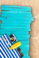 Blue and white striped towel with camera, yellow bottle, starfish, sunglasses on wooden boards, pier. Pool, beach, sea. Vertical, horizontal. Vacation, travel, relaxation. Copy space photo