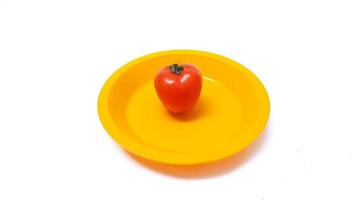 tomate en un plato amarillo aislado sobre fondo blanco foto