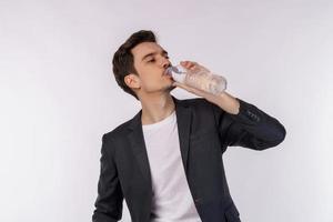 Portrait of Happy young man drinking water from a bottle and looking at camera isolated over white background photo