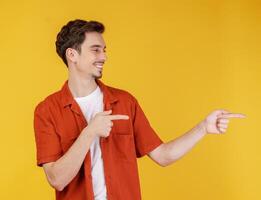 Portrait of young man pointing fingers at copy space isolated on yellow studio background photo