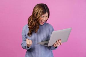 Portrait of Happy successful young woman holding laptop in her hands while standing isolated over pink background. Technology and Business concept. photo