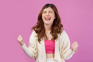 Portrait close-up of cheerful positive young woman standing and making winner gesture isolated over pink background