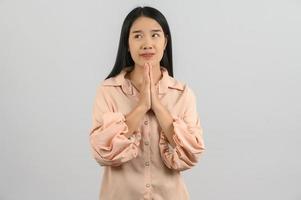 retrato de una joven asiática con camisa rosa rezando con las manos entrelazadas aisladas de fondo blanco