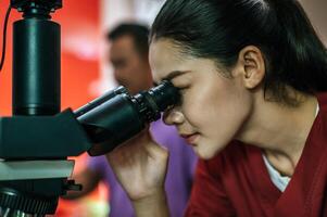 Asian young female farmer looking through a microscope in a laboratory. Modern technologies in agriculture management, agribusiness and research concept. photo