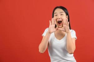 retrato de una joven asiática con una camiseta blanca que grita una historia o hace un anuncio aislado de fondo rojo