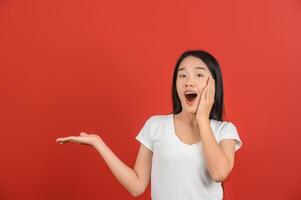 Portrait of young asian woman pointing with two hands and fingers to the side over isolated red background photo