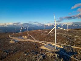 molinos de viento en las colinas durante la puesta de sol. energía renovable, energía verde. montañas en el fondo con nieve. energía eólica y respetuoso con el medio ambiente. Futuro sostenible. acabar con los combustibles fósiles. foto