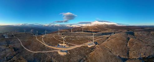 Windmills on the hills during sunset. Renewable energy, green energy. Mountains in the background with snow. Wind power and environmentally friendly. Sustainable future. End fossil fuels.