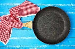 sartén redonda negra vacía con mango de madera y servilleta de cocina roja foto