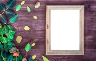 Empty wooden frame on brown wood surface among green and yellow leaves photo