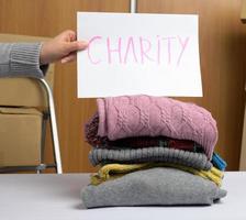 female hand holds a sheet of paper with an inscription and a stack of clothes photo