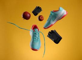 red apple, gloves and pair of textile blue sneakers with laces levitate on a yellow background. photo