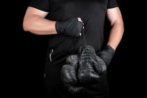 athlete in black clothes holds very old vintage leather black boxing gloves photo