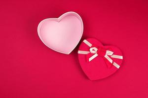 open red heart-shaped gift box with a bow on a red background photo