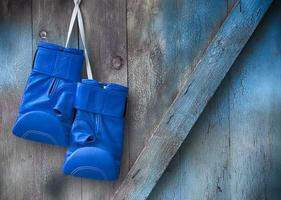 guantes de boxeo azules cuelgan de un clavo en una pared de madera en mal estado foto