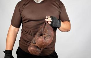 athlete in brown clothes holds very old vintage leather boxing gloves photo