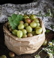 green gooseberries in a paper bag on a wooden board photo