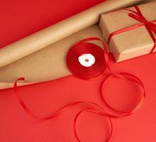 paper for packaging, a reel of red ribbon and a wrapped gift in brown kraft paper photo