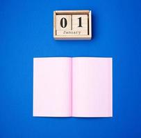 wooden retro calendar with the date of January 1 and an open notebook with empty pink sheets photo