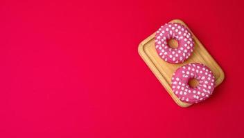 three baked round donuts in pink glaze on a red background photo