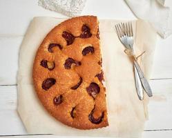 half sponge plum cake on parchment paper and two forks photo