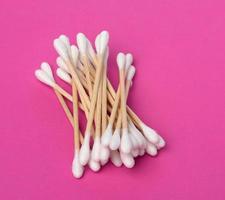 wooden sticks with white cotton wool for the ears on a pink background, hygiene product photo