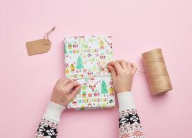 two female hands are wrapping a gift in holiday paper photo